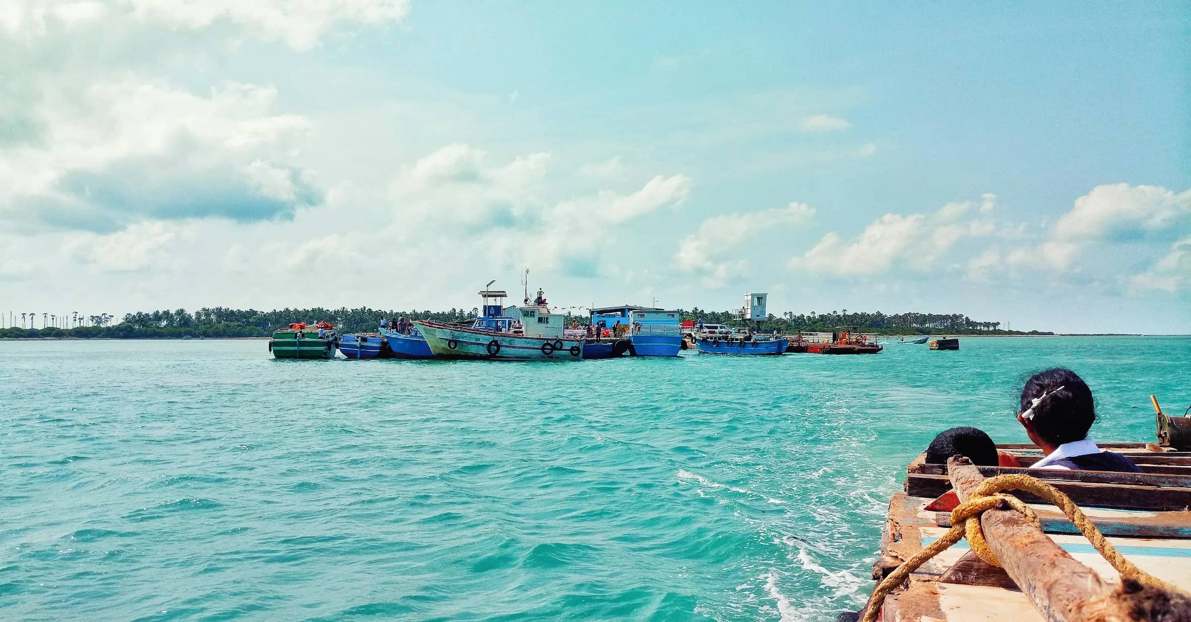 பச்சைக் கரையோரம் நிறுத்தப்பட்ட வண்ணப் படகுகளுடன் நீலப்பச்சைக் கடல்