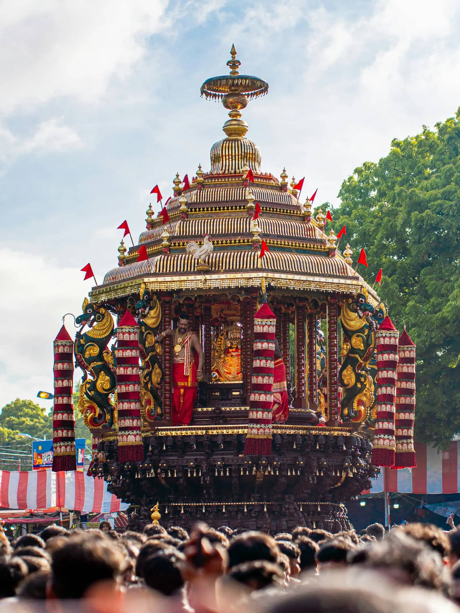 திருவிழா ஊர்வலத்தில் சிவப்புக் கொடிகளால் அலங்கரிக்கப்பட்ட கோயில் தேர்